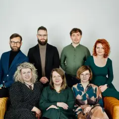 Grupa siedmiu psychoterapeutów, cztery kobiety i trzech mężczyzn, pozuje do zdjęcia na kanapie.