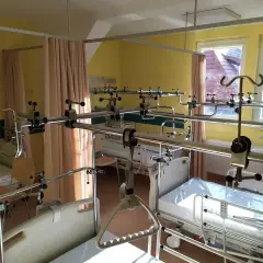 Pokój szpitalny z łóżkami i systemem poręczy nad łóżkami.