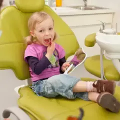 Mała dziewczynka z lusterkiem sprawdza swoje zdrowe zęby mleczne podczas wizyty u dentysty.