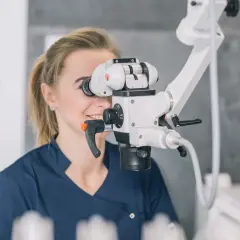 Dentystka wykonuje leczenie kanałowe pod mikroskopem, precyzyjnie pracując z użyciem nowoczesnego sprzętu.