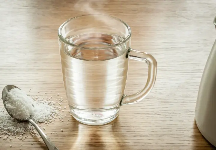 Łyżka soli i szklanka ciepłej wody, gotowe do płukania gardła solą.