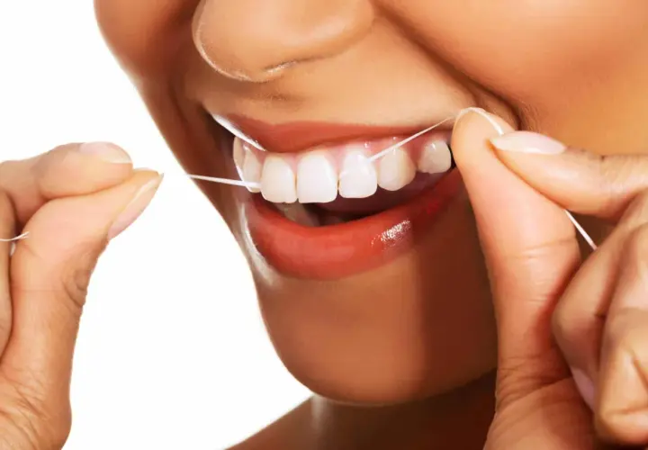 Uśmiechnięta osoba używa nić dentystyczną do czyszczenia zębów. Dbałość o higienę jamy ustnej jest ważna.